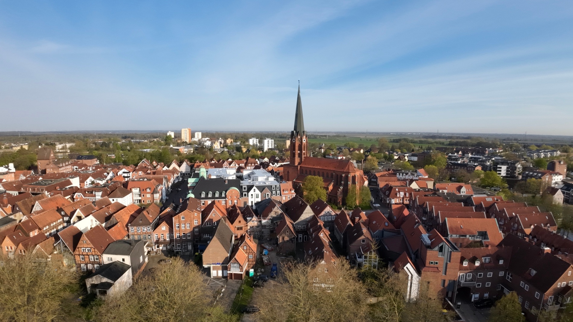 Luftaufnahme einer europäischen Stadt mit roten Dächern und hohem Kirchturm unter blauem Himmel.