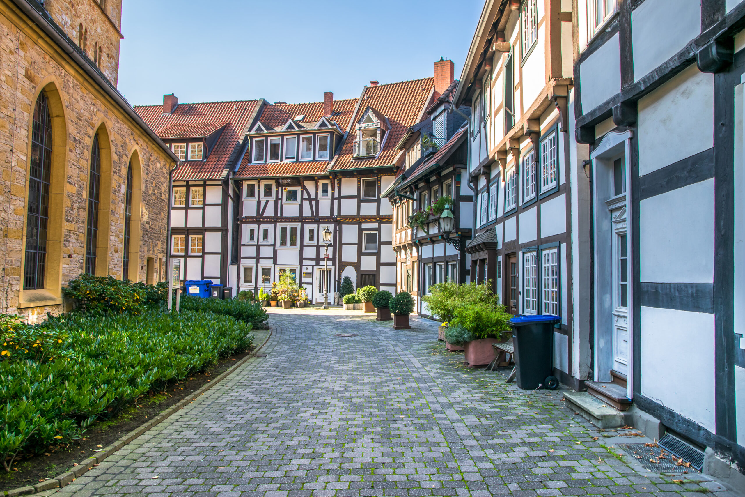 Kopfsteinpflasterstraße mit historischen Fachwerkhäusern und Grün an einem sonnigen Tag.