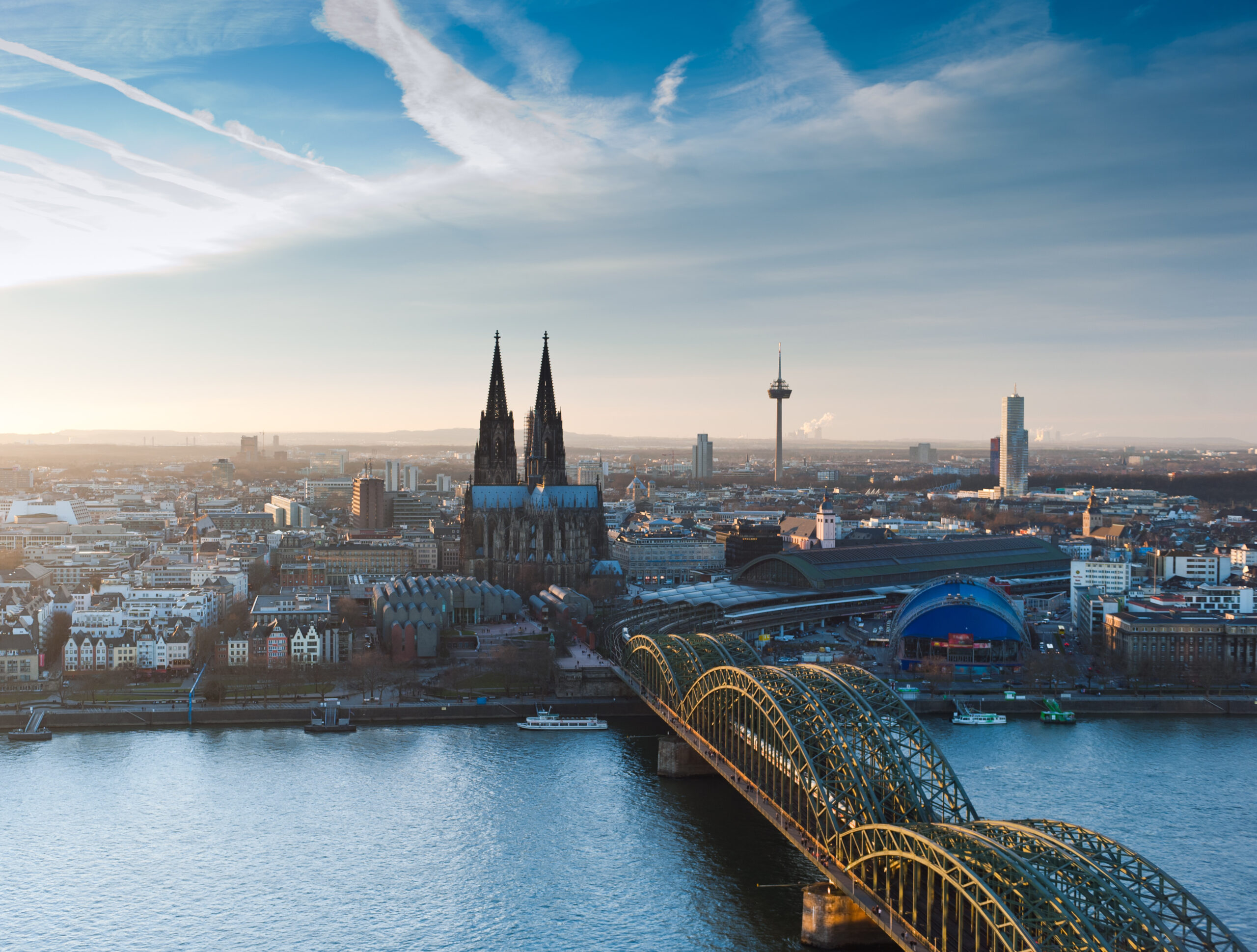 Kölner Dom mit Hohenzollernbrücke über dem Rhein unter blauem Himmel in Köln.