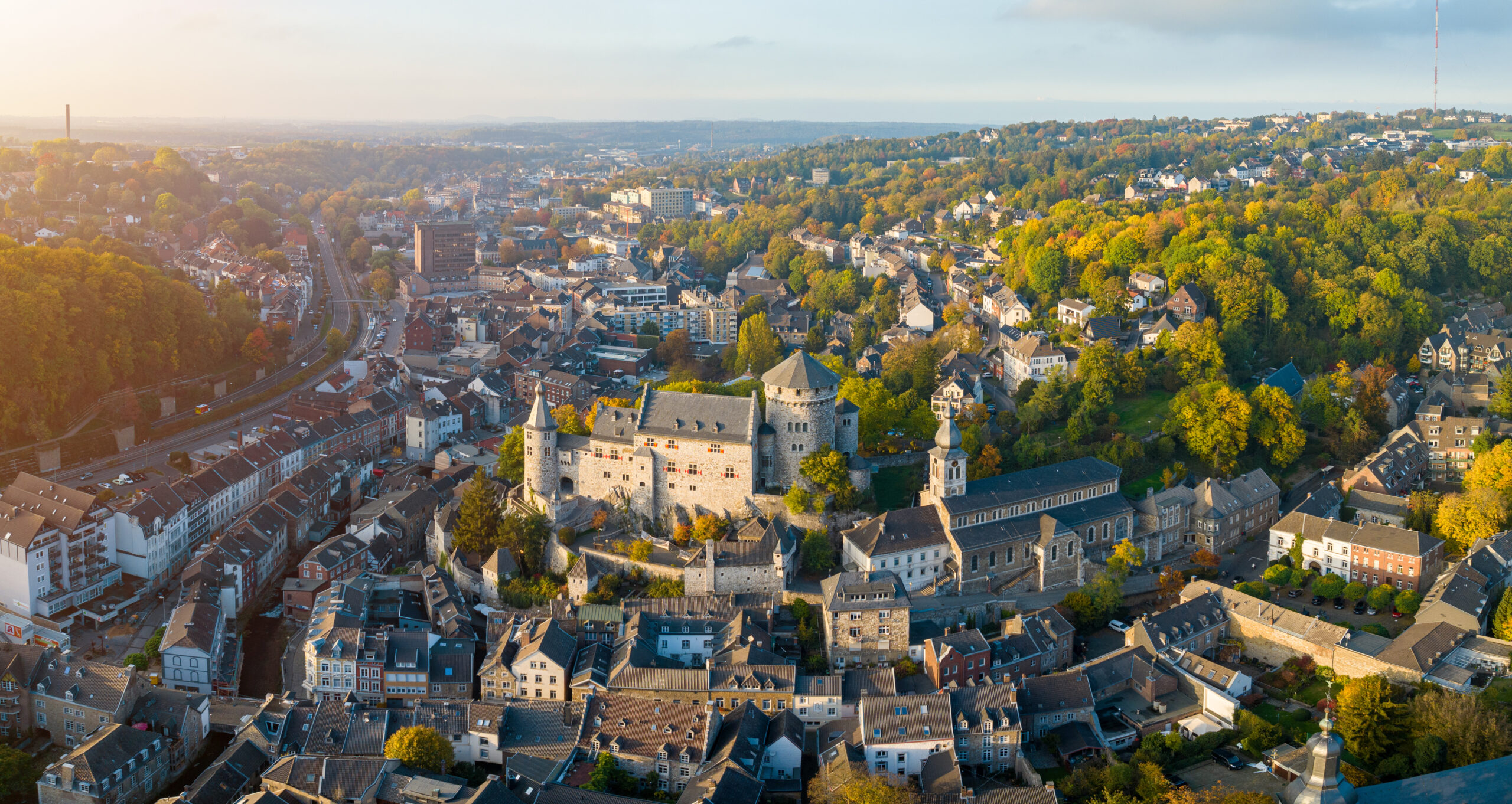 Luftaufnahme einer historischen europäischen Stadt mit Burg, Kirche und von Herbstbäumen umgebenen Gebäuden.